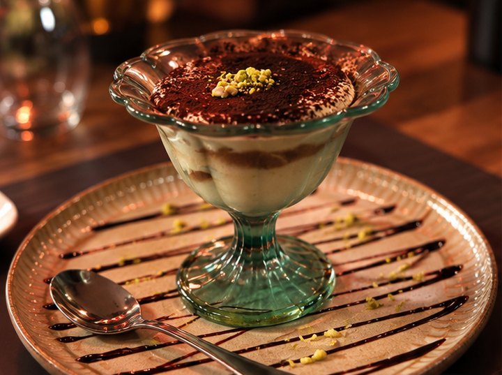 Tiramisu in een glazen coupe op een bord met chocoladesaus