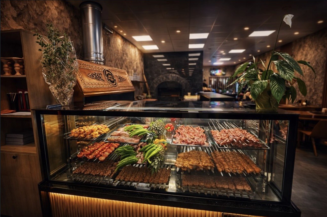 Grillvitrine van Resto 42 met spiesen, köfte, kip, groenten en pepers, met achteraan de stenen houtoven